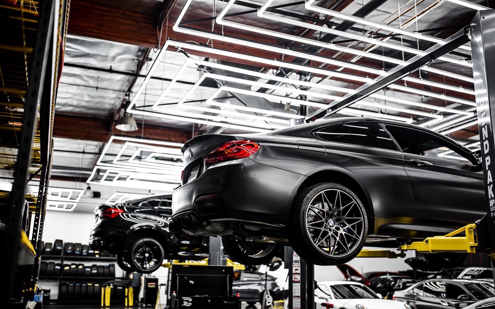A dark grey sports car raised on a hoist inside a clean, brightly lit repair shop.